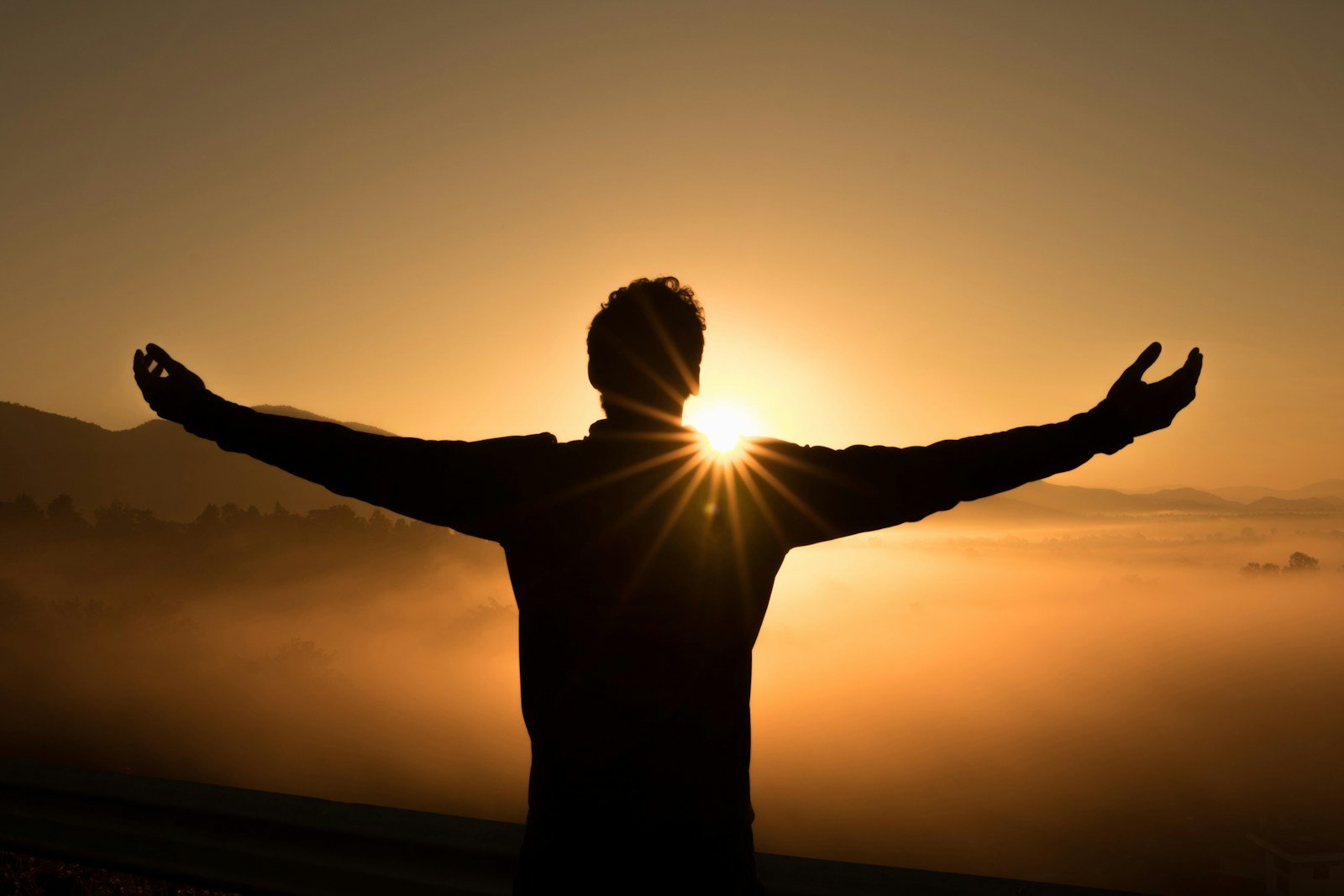 Male silhouette standing with arms outstretched facing a misty sunrise, symbolizing resilience, hope, and embracing life while managing chronic pain.