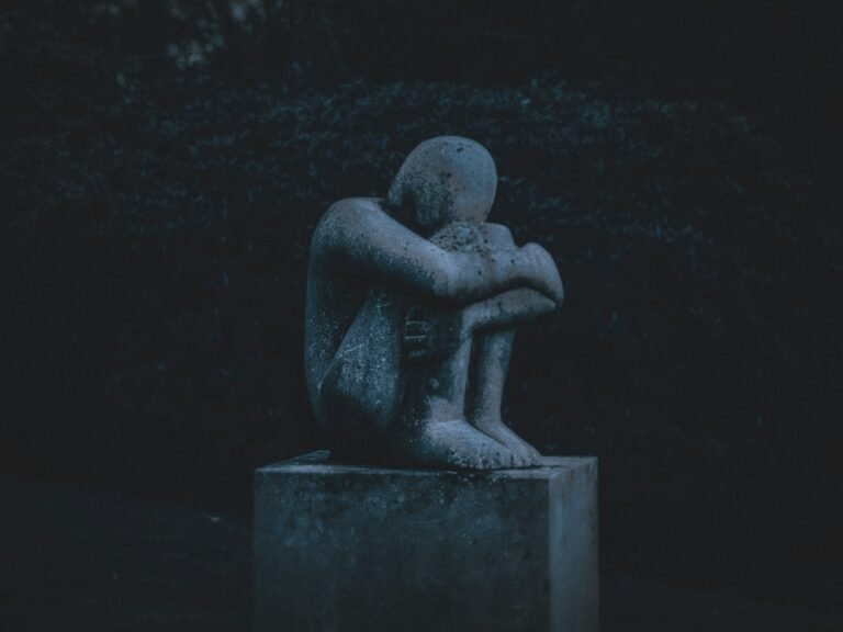 Stone statue curled up in pain, symbolizing the silent weight of chronic pain guilt.