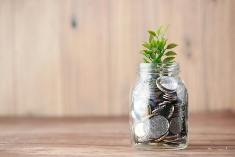 Loose change in a glass jar with a small green plant sprouting, symbolizing financial growth with chronic illness.
