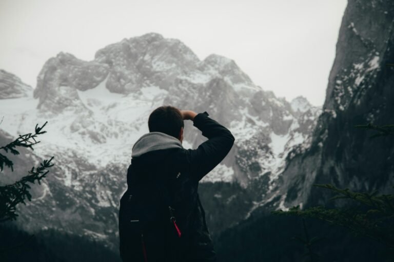 Young man with hand shading his eyes, staring up at a towering mountain — symbolizing the steep climb of investing with chronic pain.